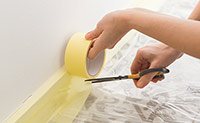 Kreppband für Maler- und Lakierarbeiten Eine Person klebt Fußleisten mit Kreppband zur Vorbereitung von Malerarbeiten ab