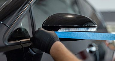 Der Ursprung des Kreppklebebandes kommt aus der Automobilindustrie In der Werkstatt wird ein Autospiegel mit Kreppklebeband abgeklebt